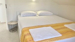 Una cama individual con ropa de cama y almohadas blancas, una mesita redonda de metal y un cabecero de madera.