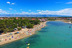 Eine Küstenstadt mit Strand, klarem, blauem Wasser und Bergen im Hintergrund.