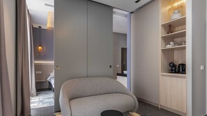 A modern living room with a sofa, a small round table, and a built-in wooden shelf with kitchen items. - Rooms Lejletul - Triple Room (Dubrovnik)