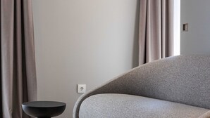 A modern living room with a grey sofa, a black side table, and a window with curtains. - Rooms Lejletul - Triple Room (Dubrovnik)