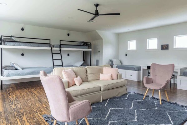 Una habitación moderna con literas, un sofá, dos sillones, un ventilador de techo y una alfombra.