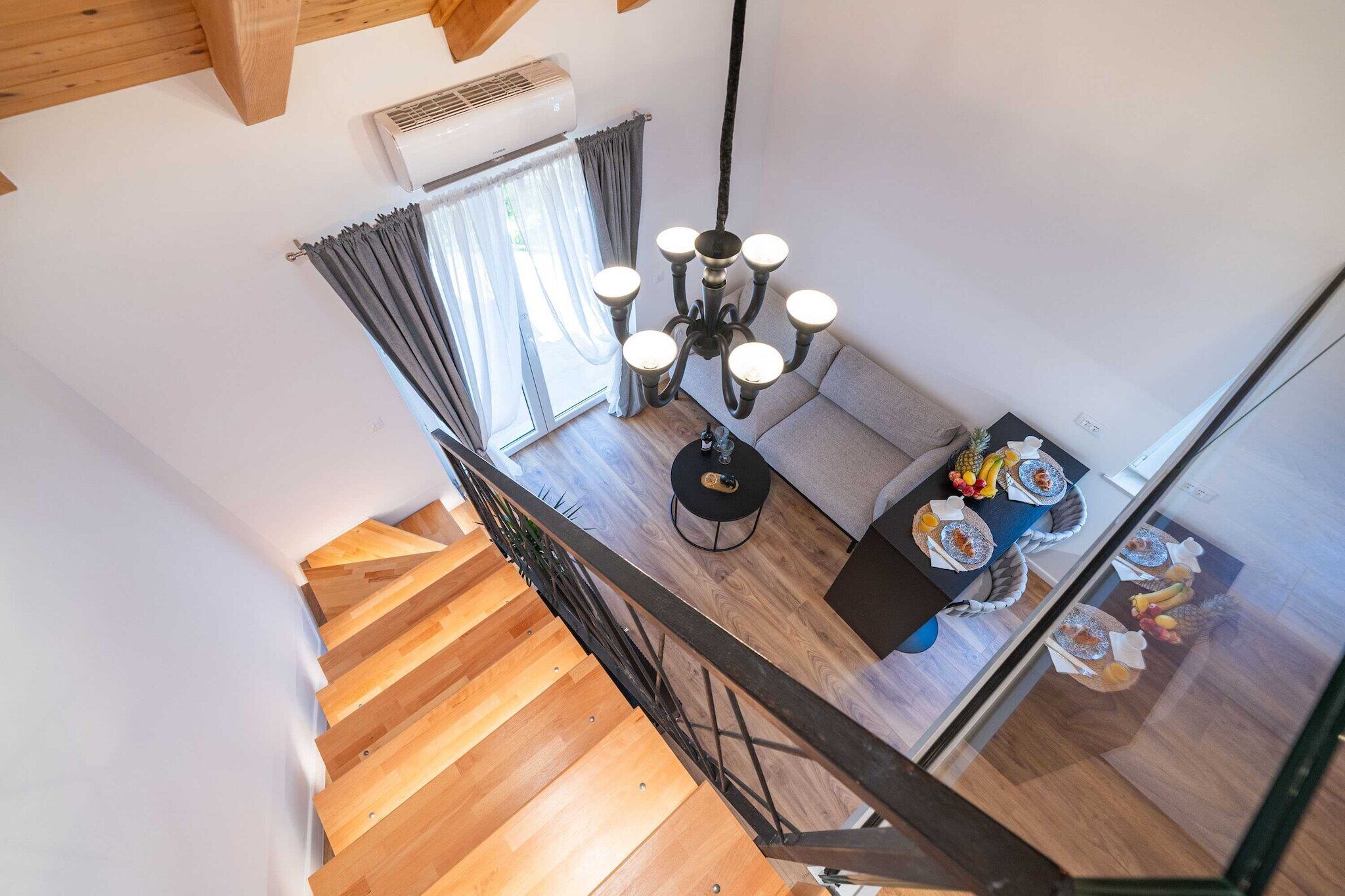 A modern interior with a wooden staircase, a chandelier, and a dining area with a table set for two.