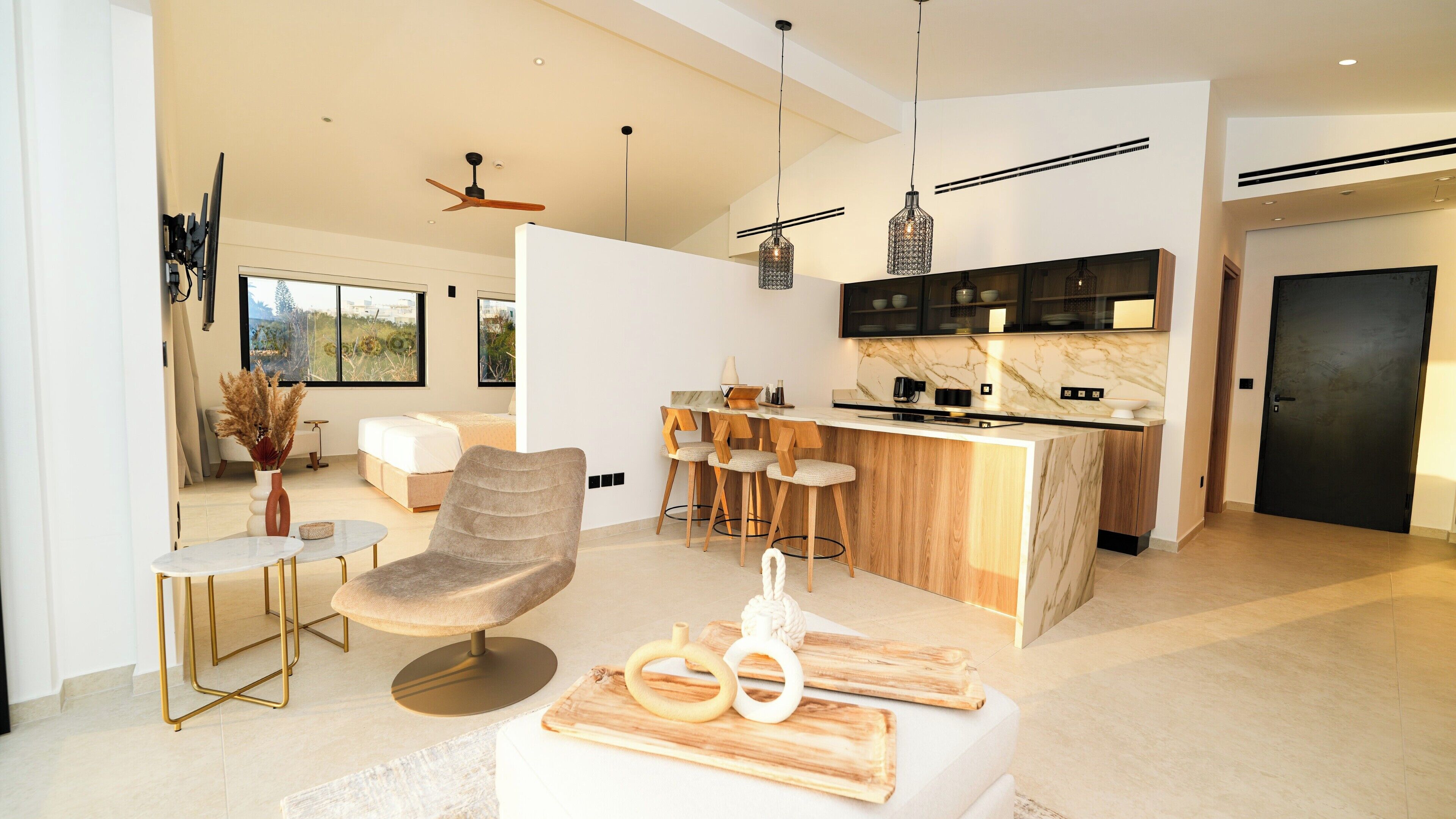 A modern living room with a sofa, a dining area with a table, and a kitchen with a marble countertop and bar stools.