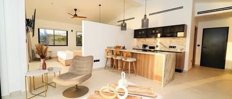 A modern living room with a sofa, a dining area with a table, and a kitchen with a marble countertop and bar stools.