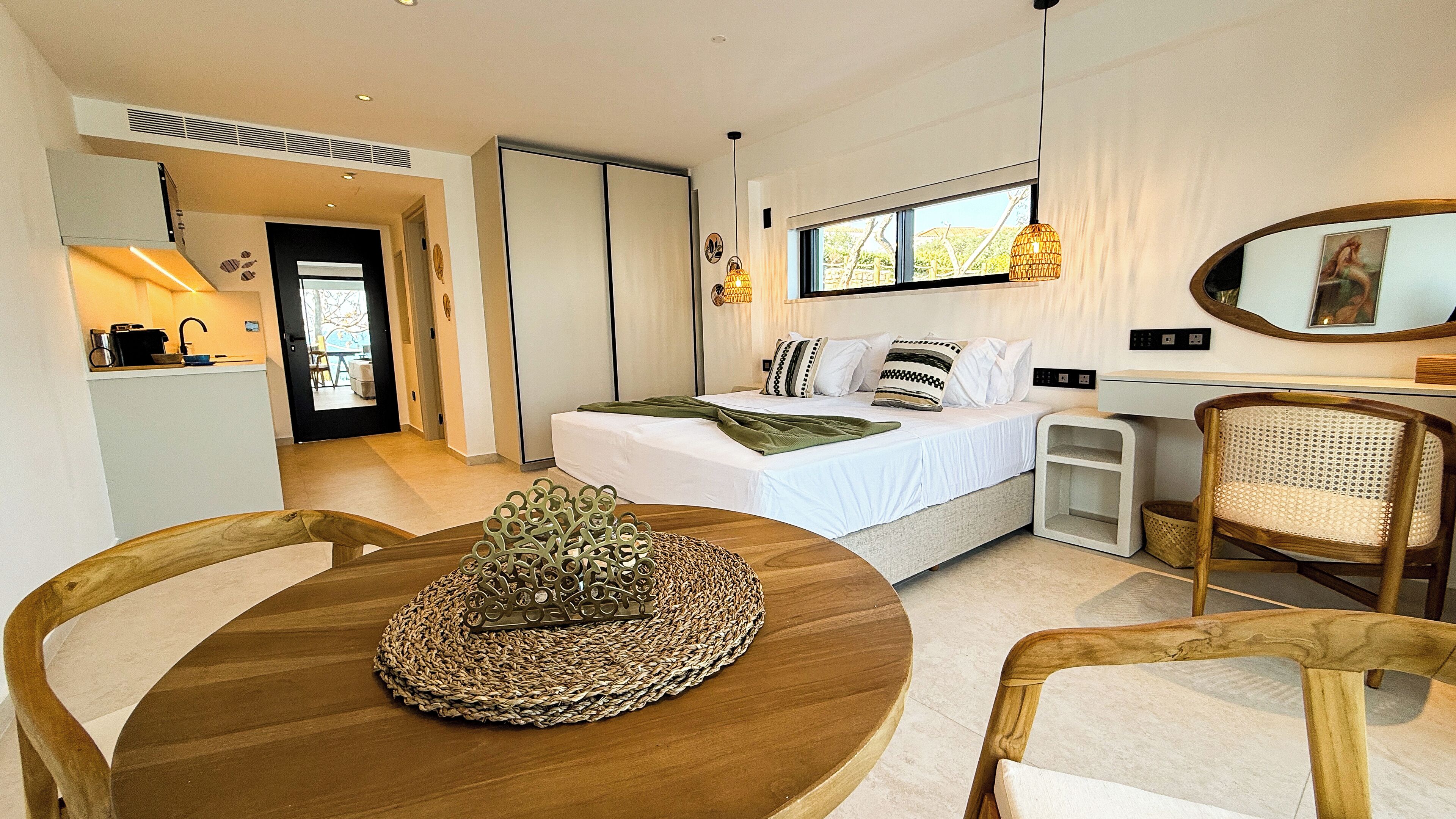 A modern bedroom with a bed, bedside tables, a desk, and a chair. There is a window with a view of trees and a door leading to a bathroom.