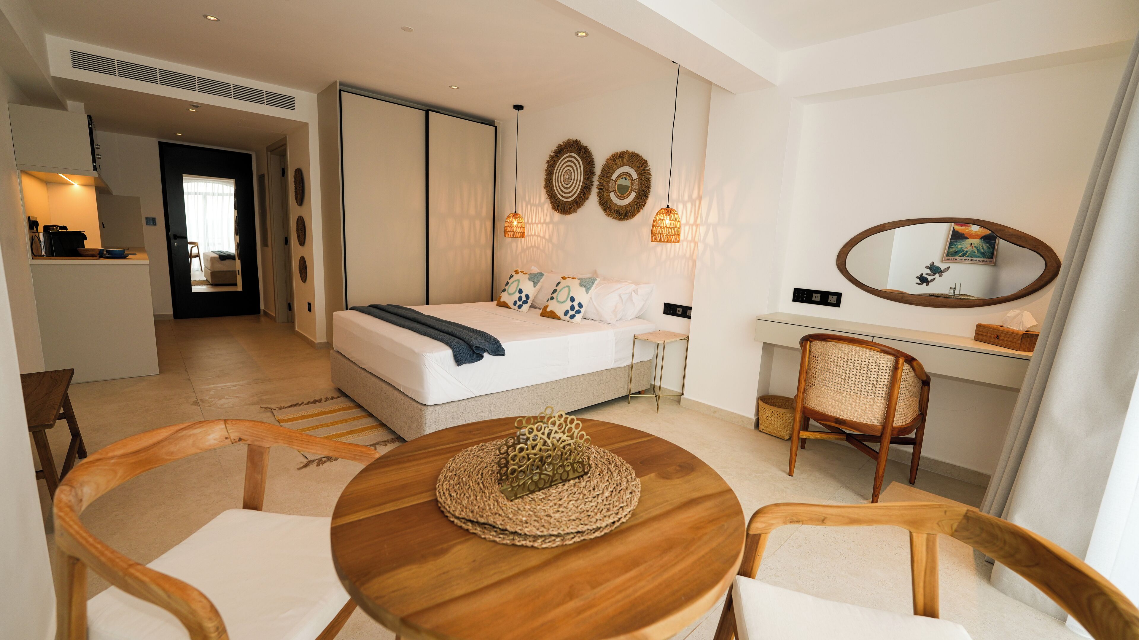 A modern hotel room with a bed, a desk, a chair, a round wooden table, and a small rug.
