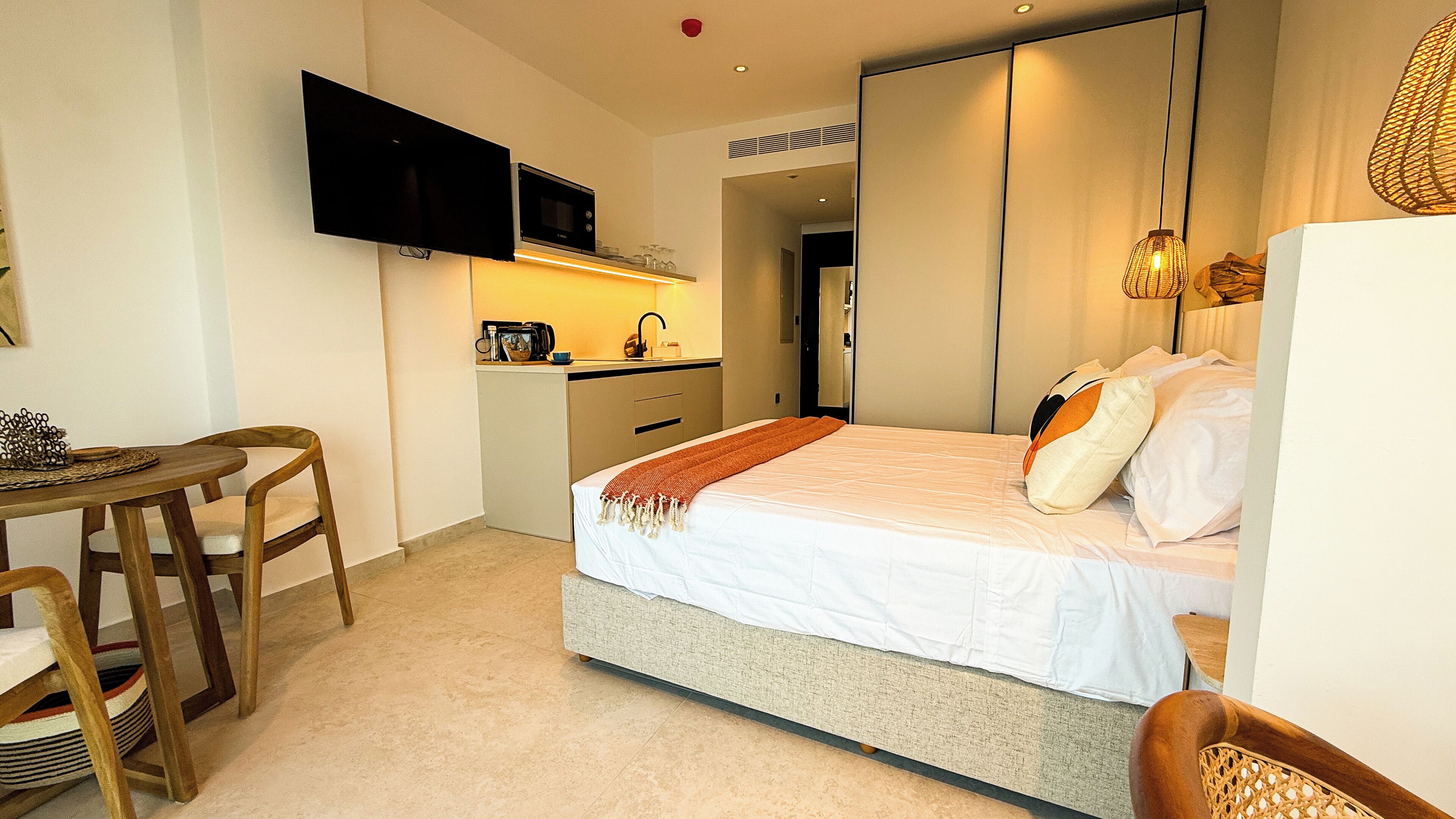 Ett kompakt hotellrum med en säng, ett litet pentry, en TV och en matplats.