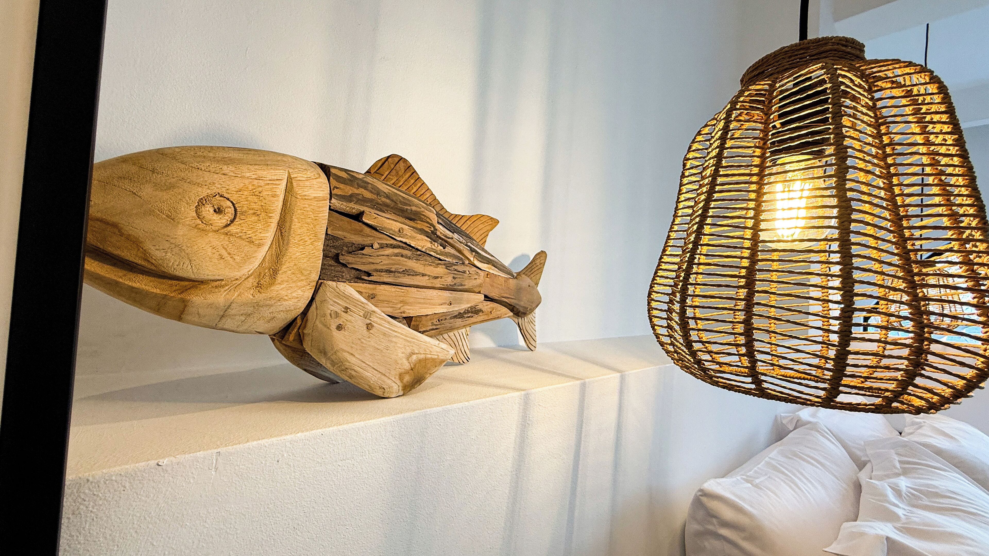 Een houten sculptuur van een vis en een geweven lamp staan opgesteld.