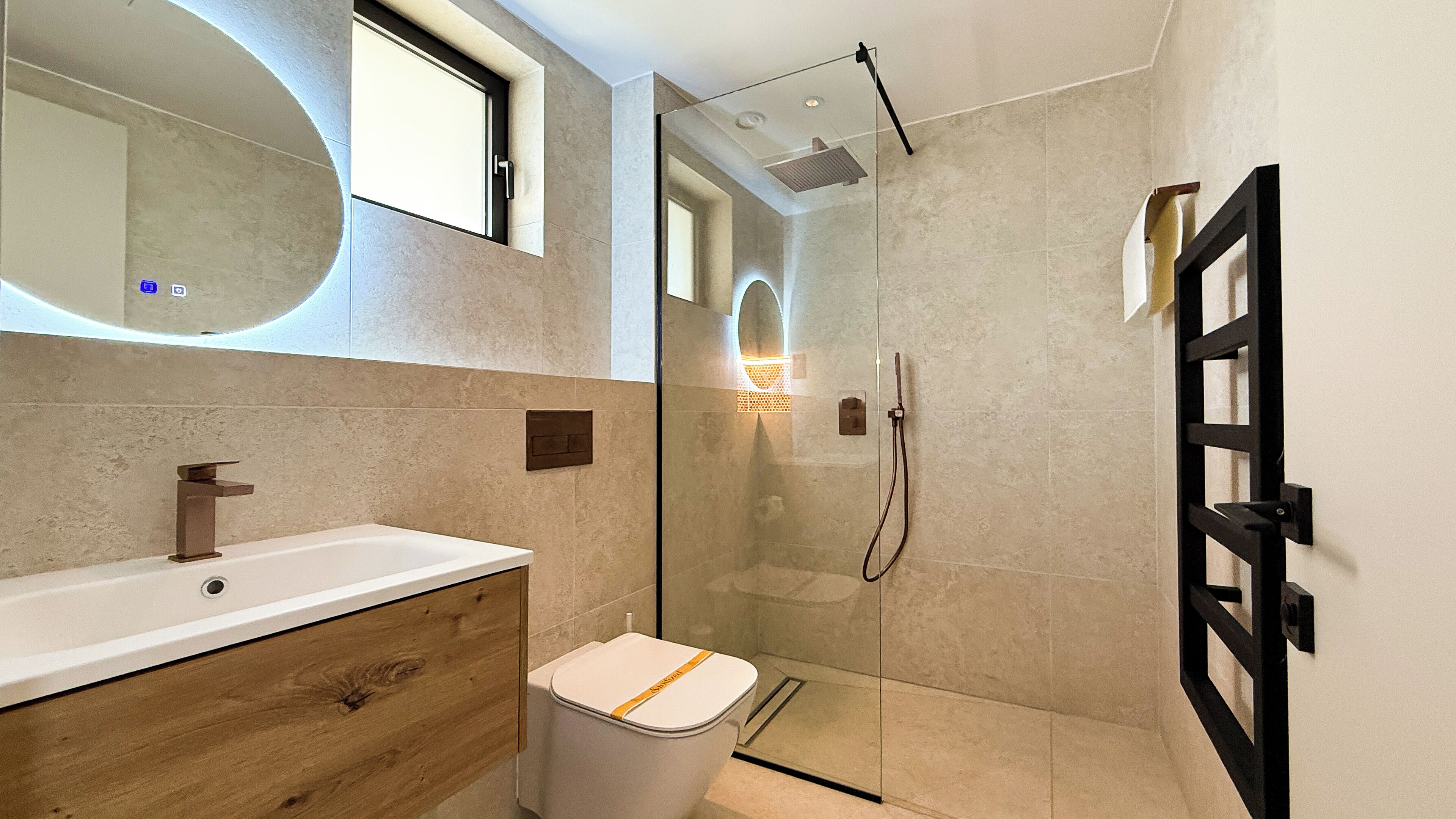 A modern bathroom with a wooden vanity, a glass shower enclosure, and a black-framed door.