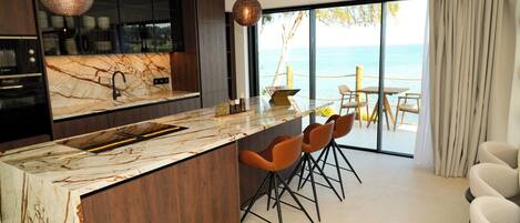Une cuisine moderne dotée d’un plan de travail en marbre, de meubles en bois foncé et offrant une vue sur la mer grâce à de grandes fenêtres.
