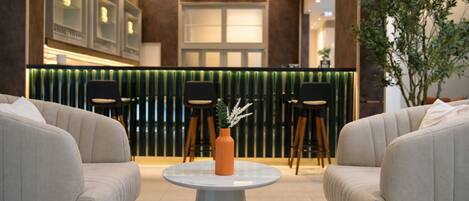 A modern lobby with a round table, two sofas, a decorative vase, and a green accent wall with vertical lines.
