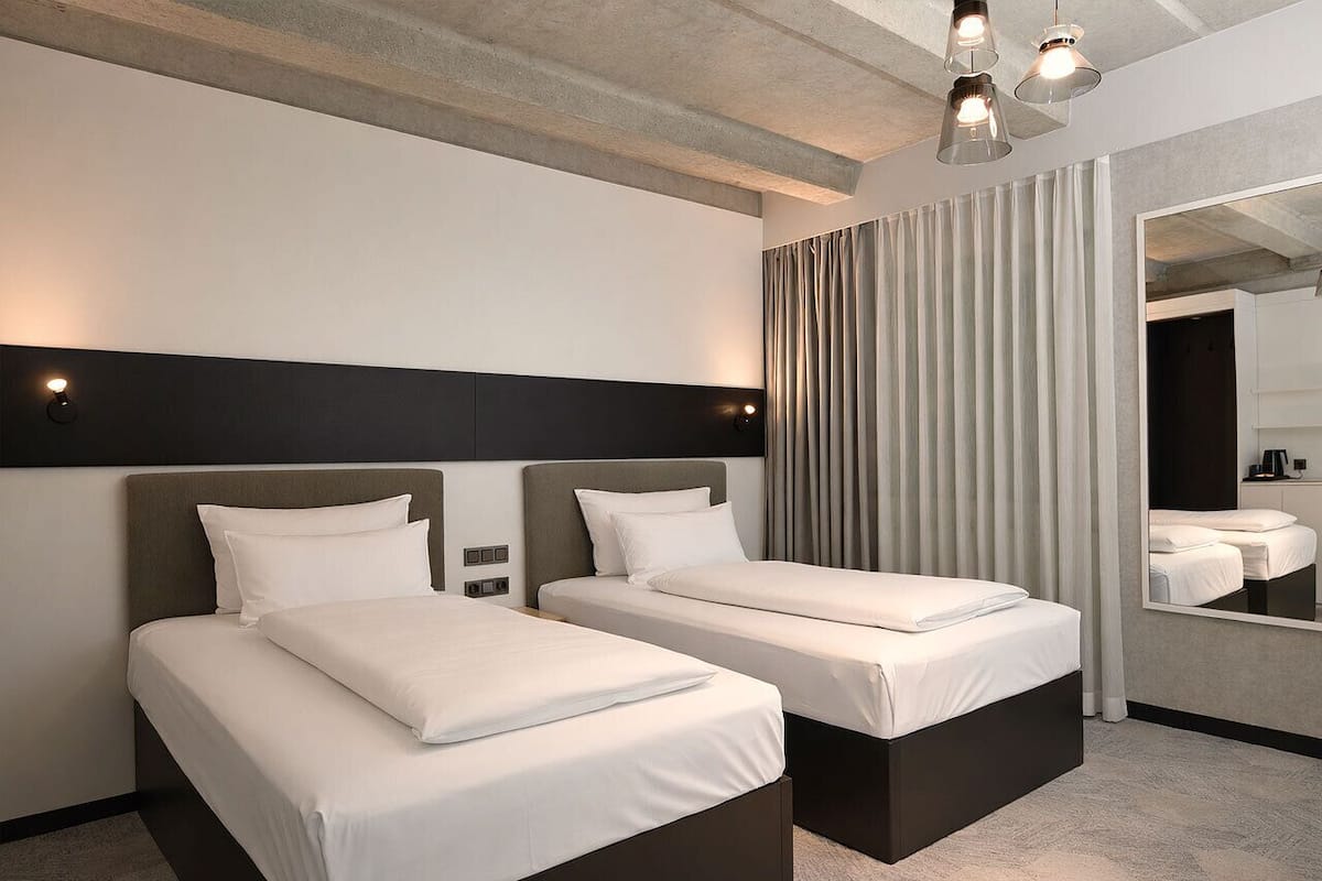 A hotel room with two beds, a large mirror, and a modern ceiling design.