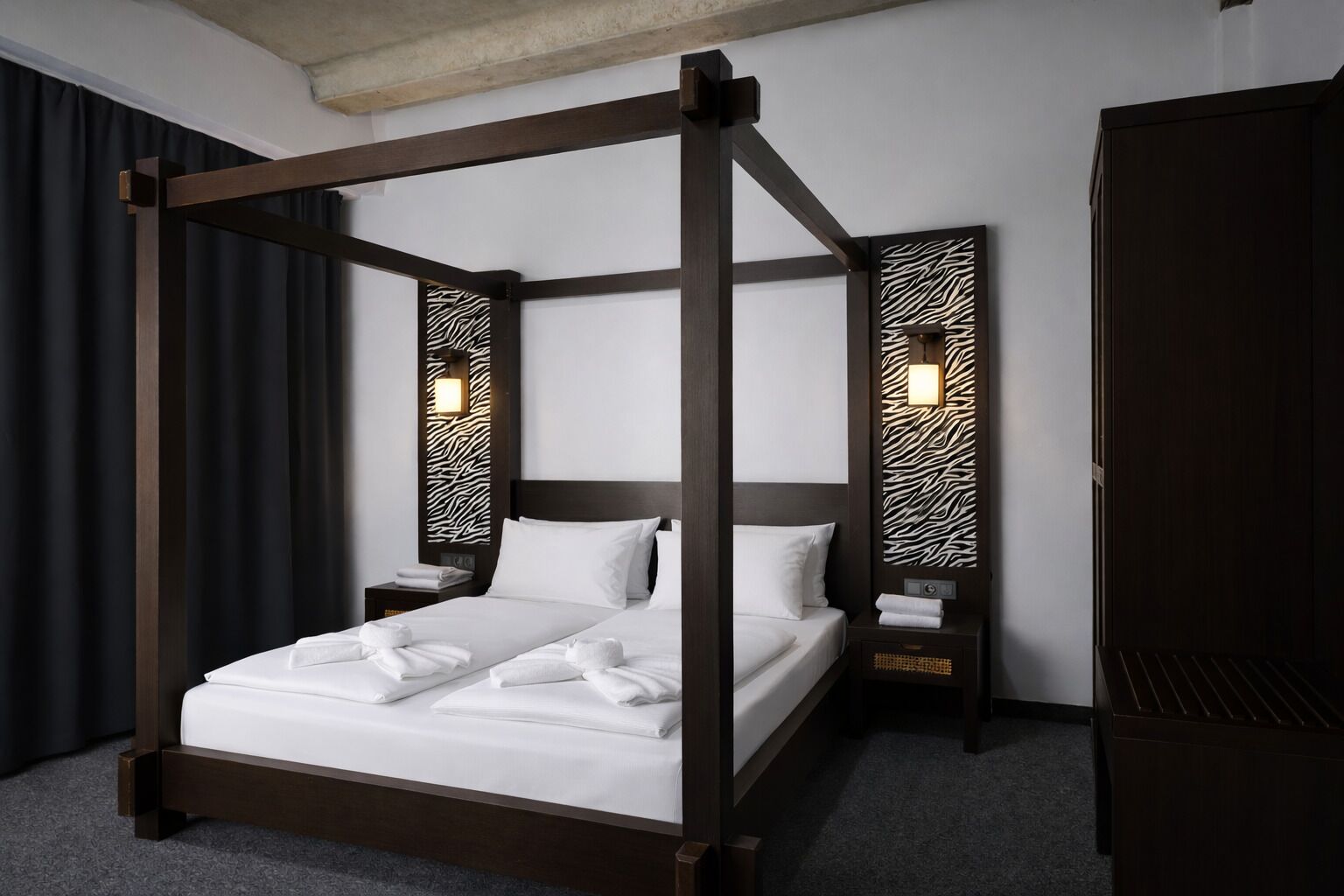 Ein Himmelsbett mit weißen Leinen und Handtüchern, zwei Nachttische mit Lampen sowie ein Kleiderschrank.