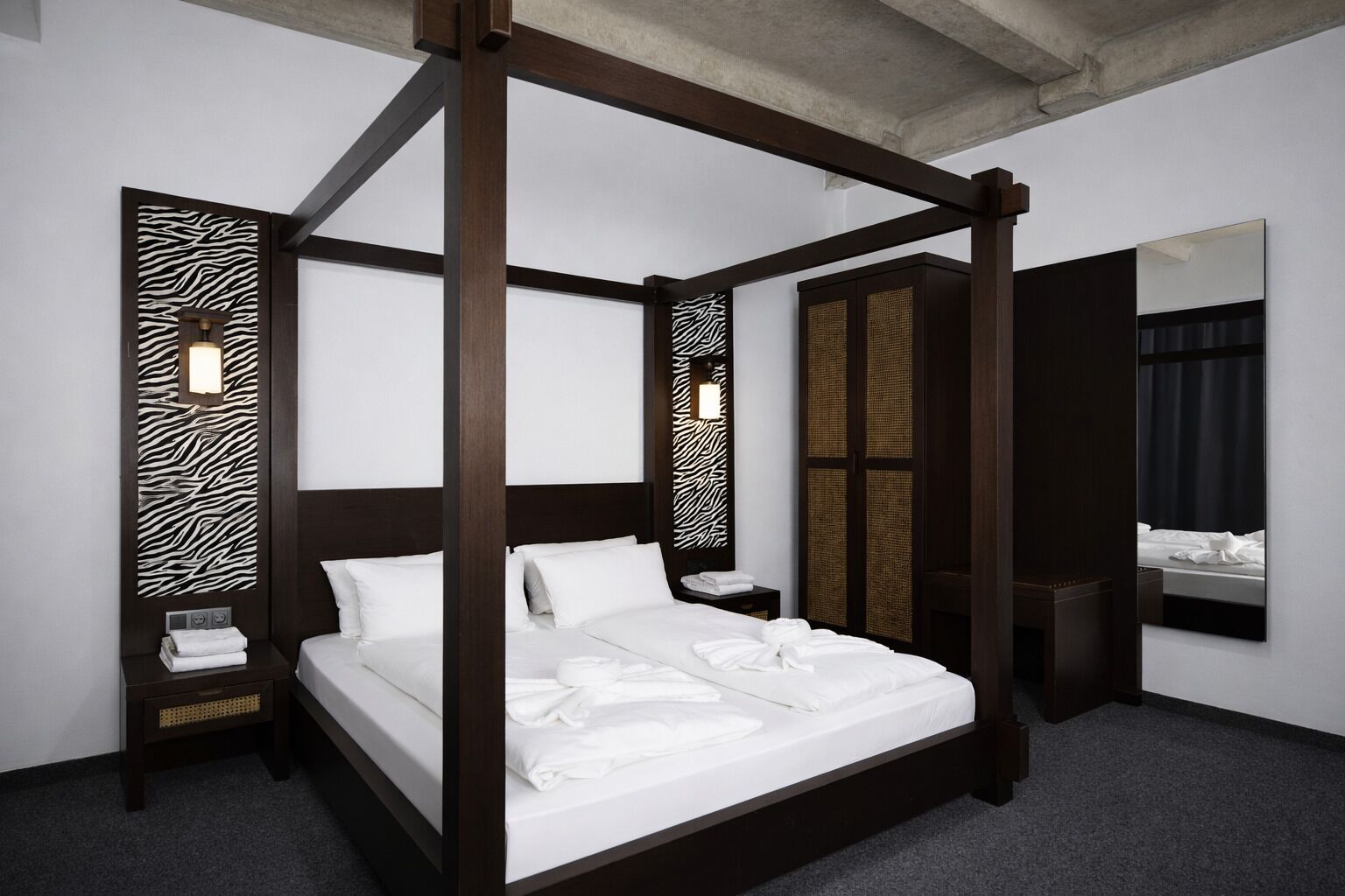 Een hemelbed met witte lakens, een nachtkastje met een lamp en een grote spiegel aan de muur.