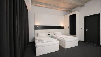 Une chambre d’hôtel moderne avec deux lits simples, une porte sombre et un mur blanc agrémenté d’un détail noir.