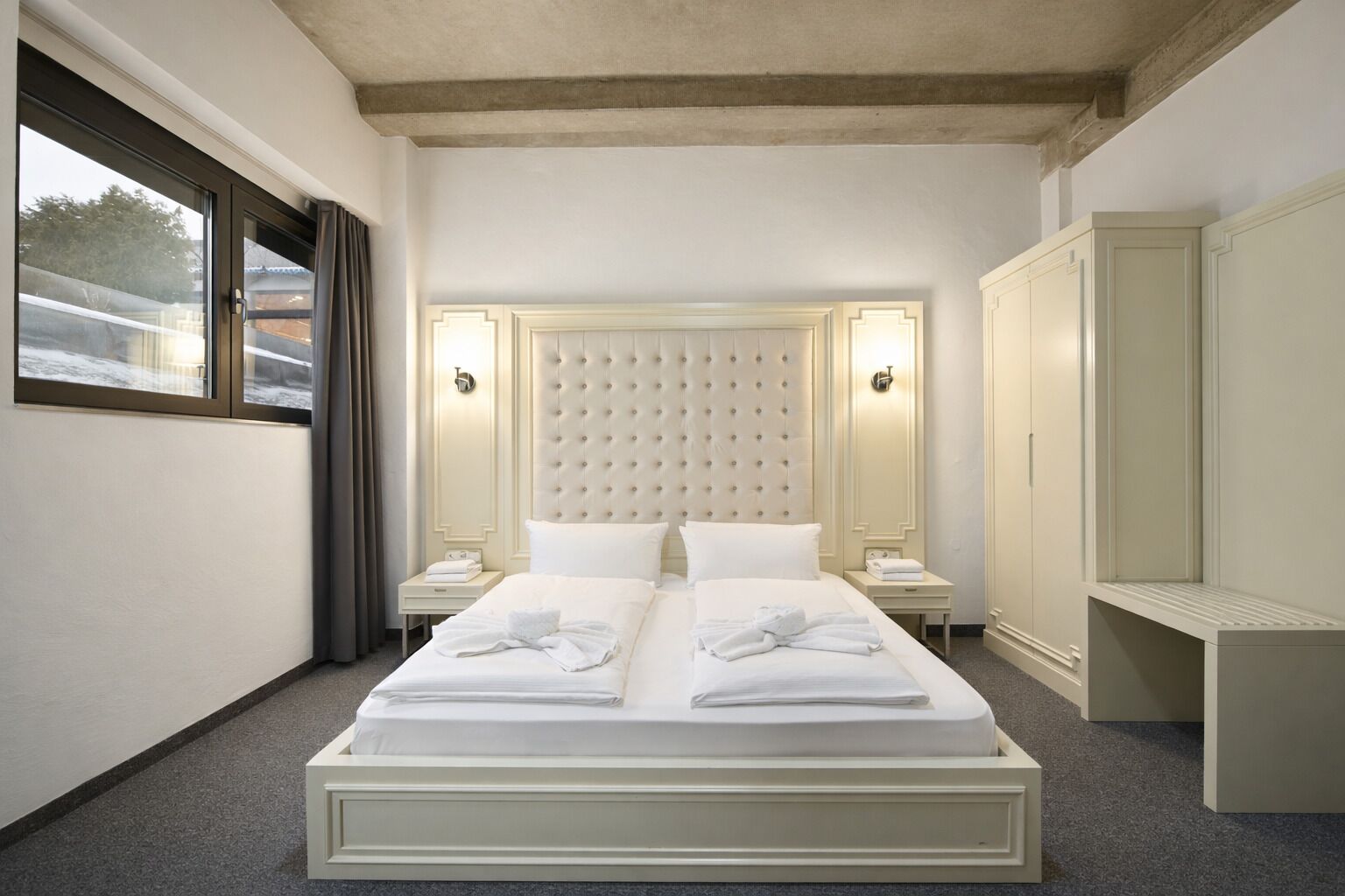 Ein Hotelzimmer mit einem großen Bett, zwei Nachttischen, einem Kleiderschrank und einem Fenster mit Vorhängen.
