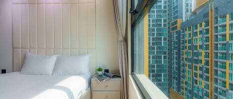 A modern hotel room with a large bed, a nightstand, and a window with a view of high-rise buildings.