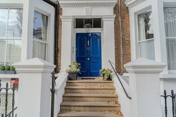 A front view of a house with a blue door, white walls, and a brick facade. - Warm & Welcoming London Escape With Home Touches (London)
