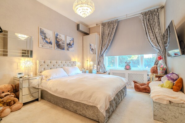 A bedroom with a large bed, bedside tables, a dresser, a mirror, and a window with curtains. - Warm & Welcoming London Escape With Home Touches (London)