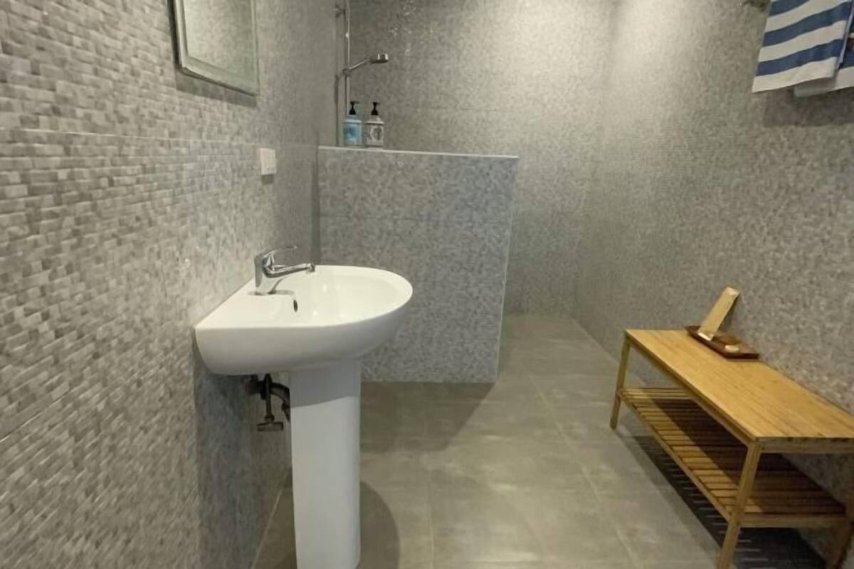 Un baño con un lavabo blanco, un banco de madera y una zona de ducha.