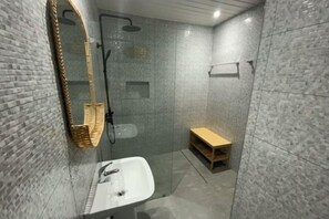 Un baño moderno con cabina de ducha de vidrio, un lavabo blanco y un estante de madera.