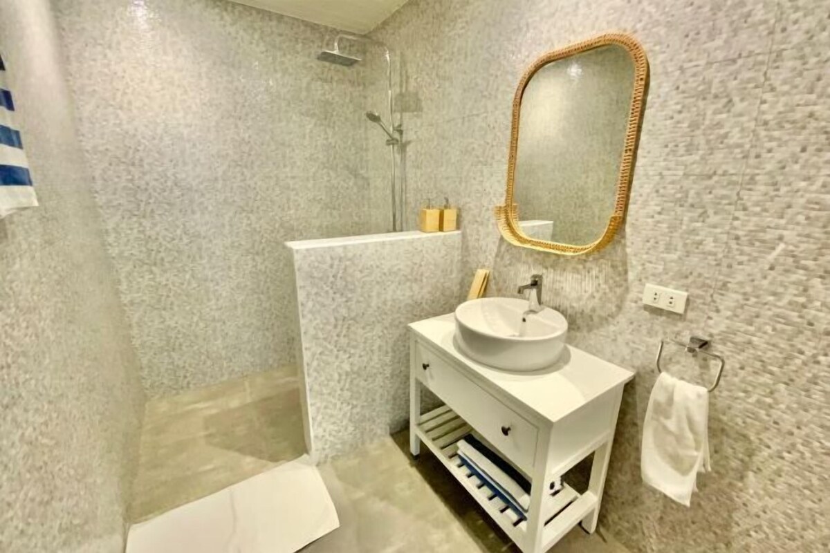 Een moderne badkamer met een witte wastafel, een rond wasbakje, een spiegel met gouden lijst en een douchehoek.