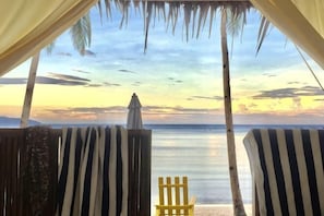 Vista a la playa desde una habitación con mobiliario a rayas y una palmera.
