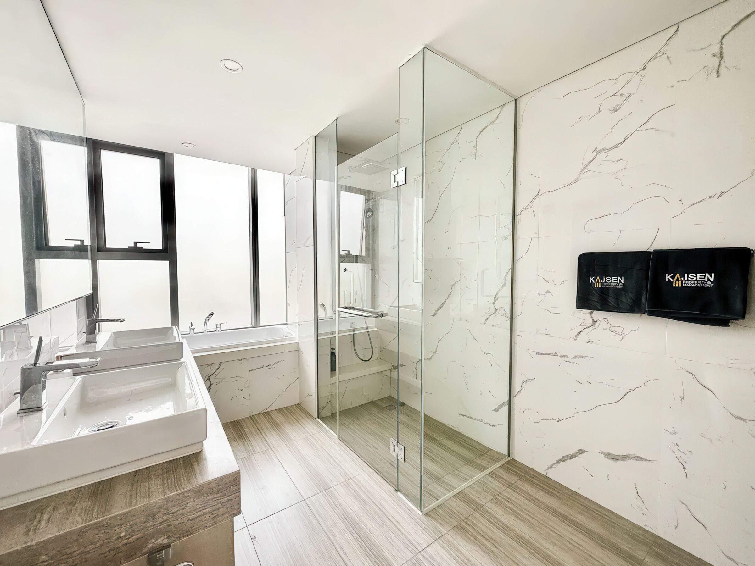 A modern bathroom with a glass-enclosed shower, marble walls, and two black storage units with the brand name 'Kajsen'.