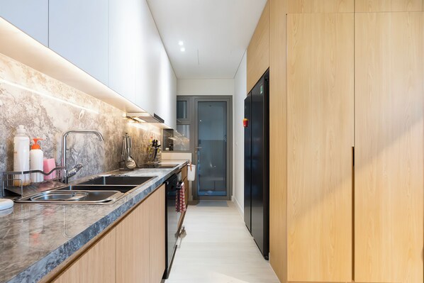 A modern kitchen with a marble countertop, stainless steel sink, and wooden cabinets.