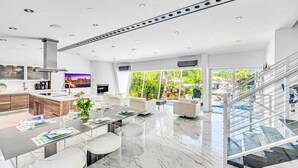 A modern kitchen with a central island, a dining area with a marble floor, and a staircase leading to a balcony with a view of a pool and greenery. - Waterfront Oasis / Cascading Pool & Views / Centrally located / Heated Pool / Cascade Key/Residences (Fort Lauderdale)