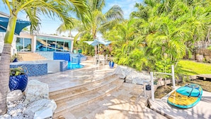 A pool area with steps leading to a lounge, surrounded by palm trees and a modern building with large windows. - Waterfront Oasis / Cascading Pool & Views / Centrally located / Heated Pool / Cascade Key/Residences (Fort Lauderdale)