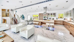 A modern kitchen with a central island, a dining area with white chairs, and a staircase leading to an upper level. - Waterfront Oasis / Cascading Pool & Views / Centrally located / Heated Pool / Cascade Key/Residences (Fort Lauderdale)