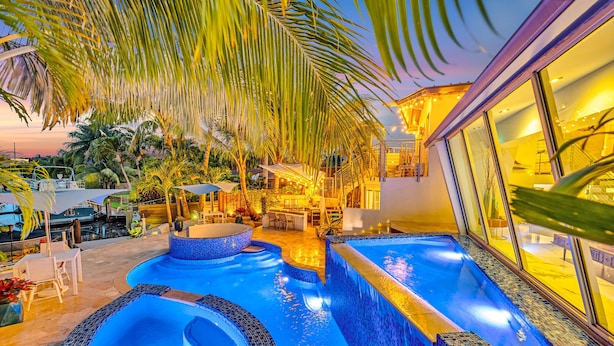 A luxurious outdoor pool area with multiple hot tubs and a seating area, surrounded by palm trees and warm lighting. - Waterfront Oasis / Cascading Pool & Views / Centrally located / Heated Pool / Cascade Key/Residences (Fort Lauderdale)