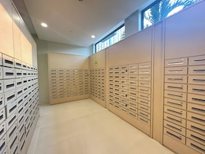 A row of metal mailboxes with labels, a tiled floor, and a window with a view of buildings. - Genius Saigon - Masteri Thao Dien District 2 (Ho Chi Minh City)