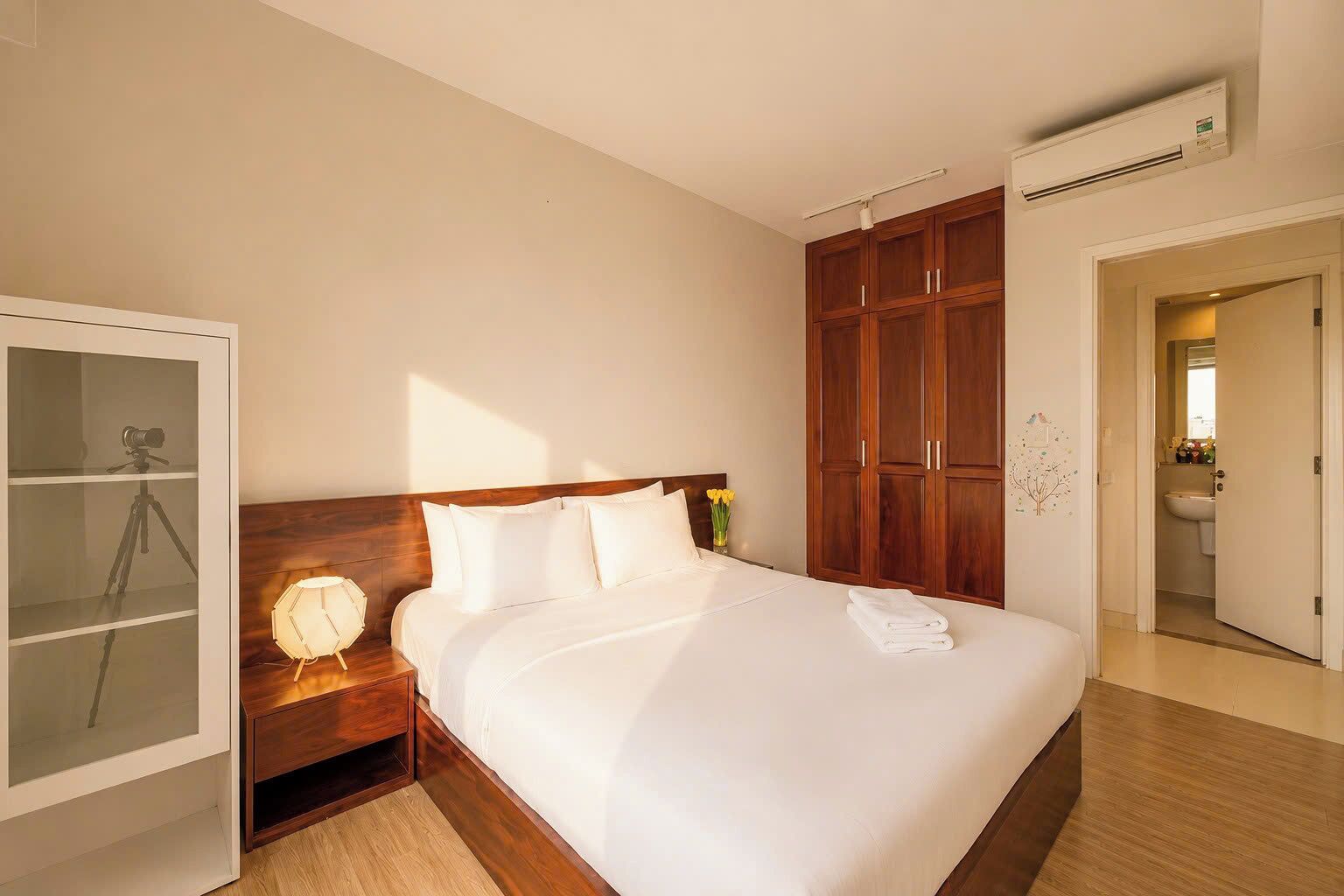 A hotel room with a bed, a wardrobe, a desk with a lamp, and an air conditioning unit.