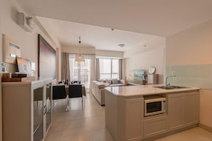 A modern kitchen with a central island, a dining area with a table and chairs, and a living room with a sofa. - Genius Saigon - Masteri Thao Dien District 2 (Ho Chi Minh City)