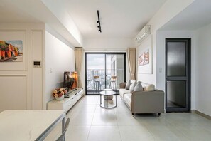 A modern living room with a sofa, a coffee table, and a TV. There is a balcony with a view of the city. - Genius Saigon - Masteri Thao Dien District 2 (Ho Chi Minh City)