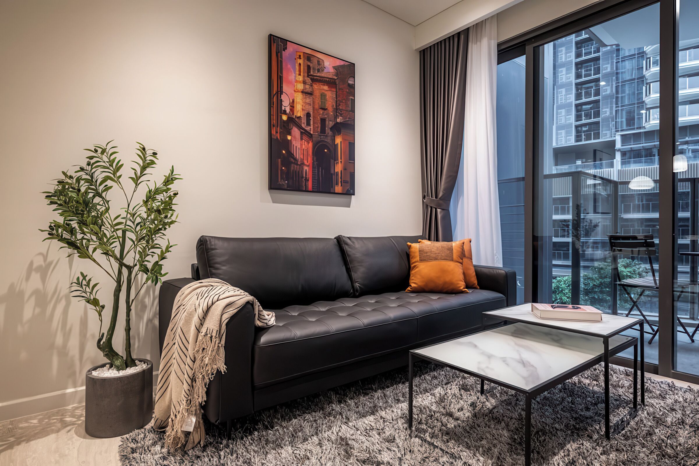 Ein modernes Wohnzimmer mit einem schwarzen Ledersofa, einem kleinen Topfpflanzen, einem weißen Couchtisch und einem großen Fenster mit Blick auf hohe Gebäude.