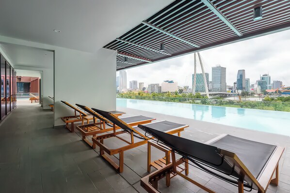 A modern hotel room with a city view, a pool, and sun loungers. - The Metropole - Horizon View Riverside  (Ho Chi Minh City)