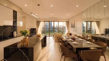 A modern dining area with a long table, multiple chairs, and a kitchen counter with a TV.