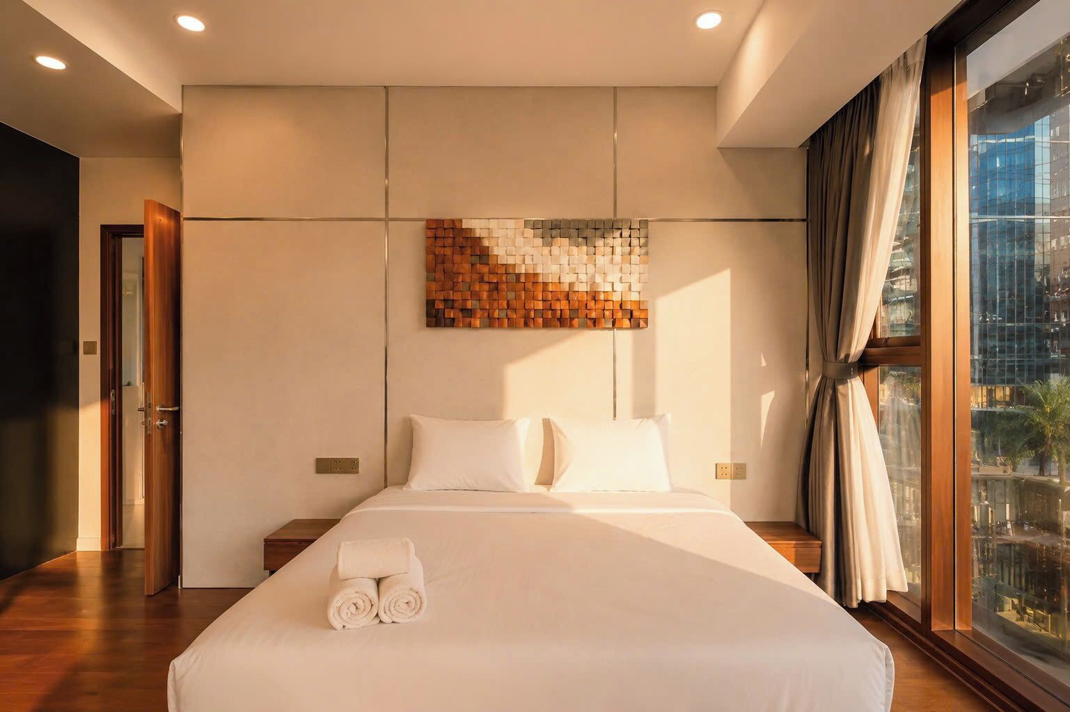 Habitación de hotel con una cama grande, una obra de arte en la pared, una ventana con cortinas y vistas a la ciudad.