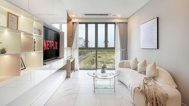 Una sala de estar moderna con una televisión de pantalla plana, un sofá, una mesa de centro y vistas de un paisaje urbano a través de amplias ventanas.