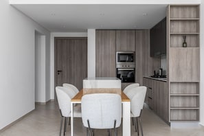 A modern kitchen with a wooden table and chairs, built-in appliances, and a wooden shelving unit.