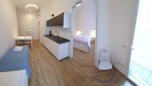 A compact hotel room with a kitchenette, a bed, a small table with chairs, and a window. - Apartment 4 (Milano)