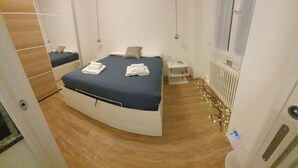 A modern bedroom with a curved bed, a bedside table, a radiator, and a mirror. - Apartment 4 (Milano)