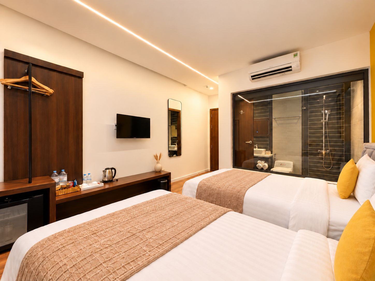 A modern hotel room with two beds, a TV, a mirror, a shower, and a minibar.