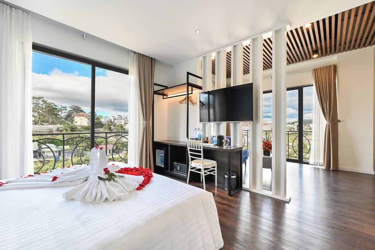 A hotel room with a large bed, a desk, a TV, and a balcony with a view.