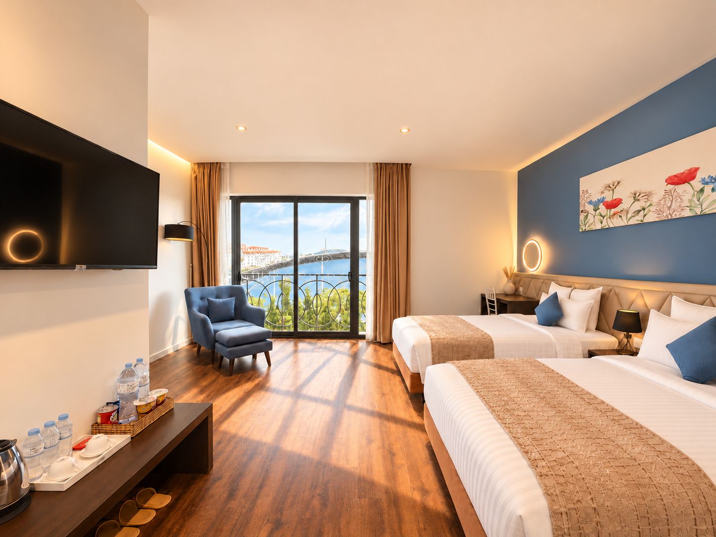 Habitación de hotel con una cama grande, una cama más pequeña, un escritorio con una silla, un televisor y vistas a un puente y al agua.