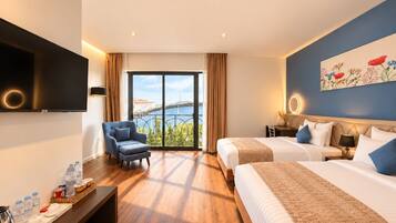 Habitación de hotel con una cama grande, una cama más pequeña, un escritorio con una silla, un televisor y vistas a un puente y al agua.