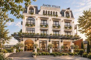 Un hotel a più piani dall'architettura classica, con un ingresso imponente, gradini, ampie finestre e un balcone adornato da piante.